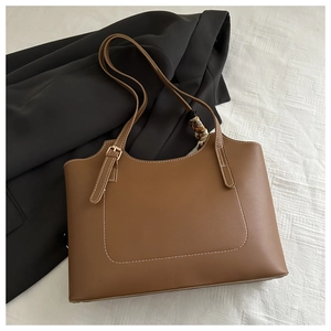 Detail of brown faux leather tote bag with contrast white stitching and gold buckles