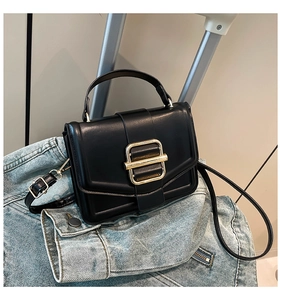 Detail of black leather crossbody bag with a large gold square buckle on a denim jacket