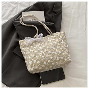 Close-up of beige woven tote bag with white flower embroidery and lace bow detail