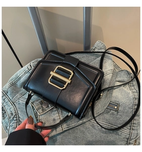 Detail of black leather crossbody bag with gold metal buckle on a denim jacket