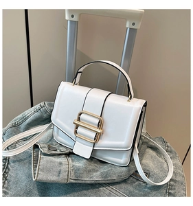 White minimalist handbag with gold metal buckle shown against denim jacket and luggage