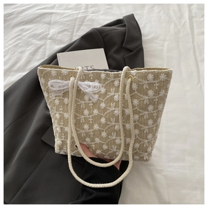 Minimalist straw tote bag with white flower embroidery and lace bow on a white bed