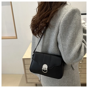 Close-up of black matte leather shoulder bag with silver metal buckle on a grey blazer