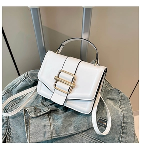 Close-up of white leather square bag featuring a large gold buckle and black piping detail