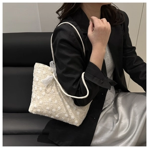 Detail of floral texture and lace bow on a beige woven tote bag held by a model