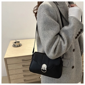 Detail of a black leather crossbody bag featuring a round silver metal buckle on a grey coat