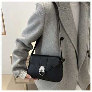 Detail of a black leather flap bag with silver metallic buckle on a grey blazer outfit