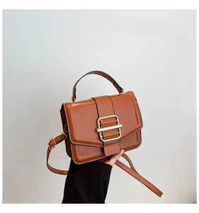 Detail of caramel brown crossbody bag with gold metallic buckle and matte leather texture