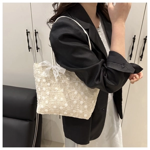 Gros plan du sac cabas beige tressé avec broderie florale et nœud en dentelle blanche