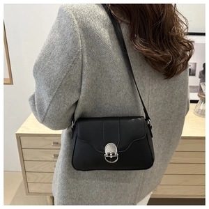 Detail of a black matte leather crossbody bag with silver oval lock on a grey coat