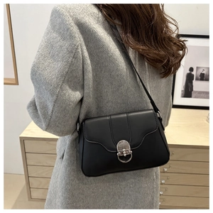 Detail of black crossbody bag featuring a silver U-shaped metal buckle on a grey coat