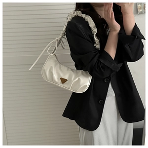 Close-up of white pleated hobo bag featuring ruffled strap and metallic triangle plaque