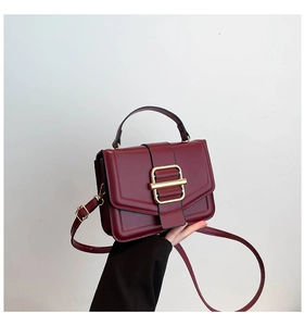 Close-up of wine red leather handbag with vintage gold square buckle and handle