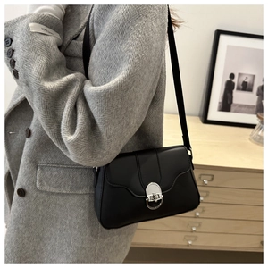 Detail view of black leather shoulder bag with sleek silver ring lock on minimalist flap