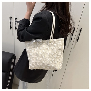 Detailed close-up of white woven tote bag with lace bow and floral embroidery details