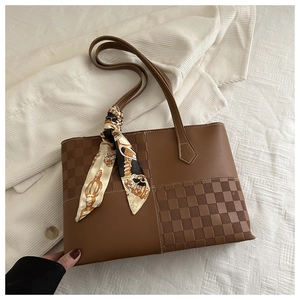 Detail of a brown leather tote bag with plaid texture and a decorative floral silk scarf