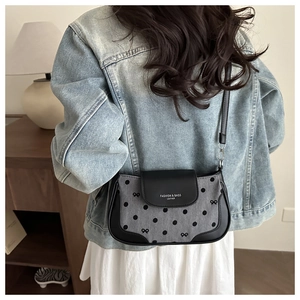 Sac bandoulière à pois et nœud avec bordure en cuir porté par un mannequin en tenue décontractée