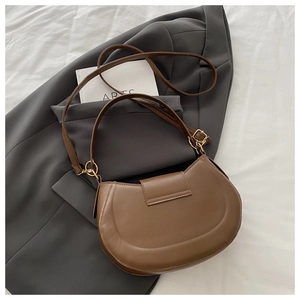 Close-up of brown saddle bag in matte leather featuring polished gold hardware accents