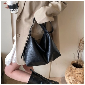 Detail of a black textured leather tote bag with an adjustable strap on a female model