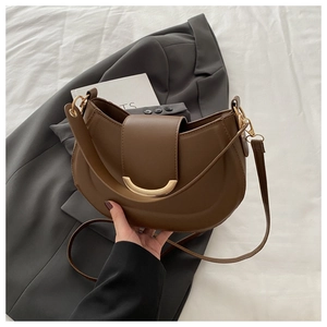Detail of a brown leather crescent handbag with a gold buckle on a stylish blazer coat