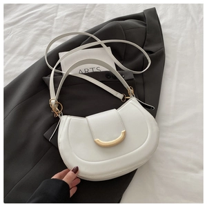 Detailed shot of white leather saddle bag with gold crescent buckle on a minimal background