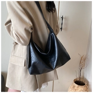 Detail of the soft leather texture on a large black crossbody tote bag worn by a model