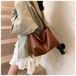 Deep brown large capacity faux leather hobo bag worn by model in a vintage urban setting