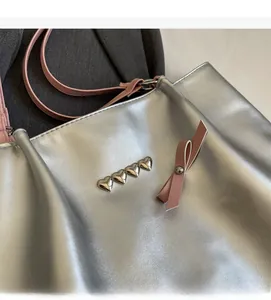 Detail of silver tote bag featuring heart rivets and a decorative pink ribbon bow