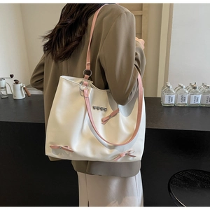 Detail of cream tote bag with pink bow accents and silver heart buckles on a model