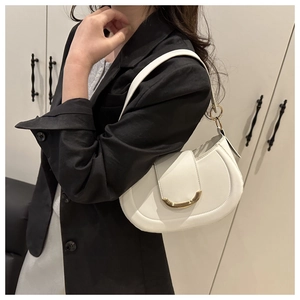 Close-up of white leather shoulder bag with gold crescent buckle on black blazer