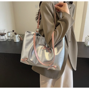 Close-up of silver metallic tote bag with pink bows and heart charms on a shoulder strap
