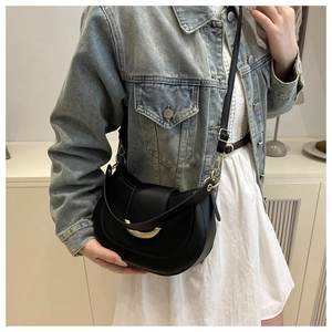Detail of black crescent crossbody bag showing golden buckle and faux leather texture