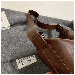 Close-up of vintage dark brown leather tote bag with brand label and metal buckle detail