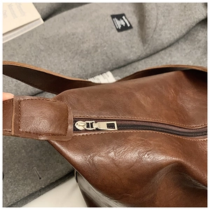 Close-up of deep brown glossy PU leather tote bag with silver zipper and textured surface
