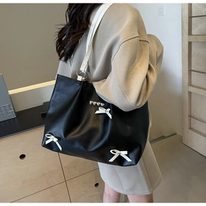 Detail of black leather tote bag featuring white bows and heart rivets on a shoulder strap