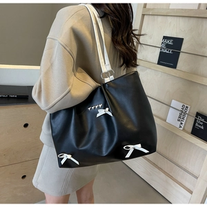 Detail of a black leather tote bag with white bows and silver heart metal accents
