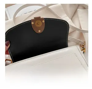 Detail view of the vintage bronze magnetic buckle on a white faux leather crossbody bag
