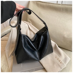 Detail of a black matte vintage tote bag with adjustable strap placed on a suit jacket