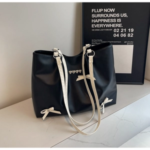 Detail of black tote bag with silver heart studs, white bows, and thin straps