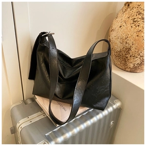 Detail of black soft leather tote bag with silver buckle on a vintage suitcase background