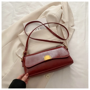 Macro shot of dark red vintage baguette bag with gold clasp on white cloth backdrop