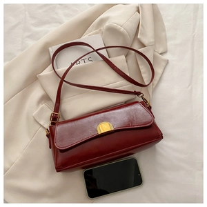 Detail of burgundy baguette bag with gold buckle on beige blazer next to a book