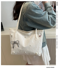 Détail du sac cabas blanc texturé avec perles, nœud argenté et pendentif cœur rose