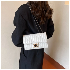 Détail d'un petit sac blanc matelassé avec boucle florale dorée porté à l'épaule