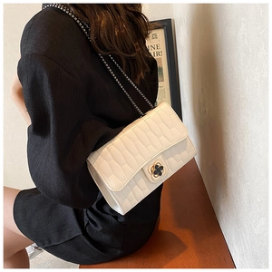 Détail d'un sac matelassé blanc avec fermoir trèfle noir et bandoulière en chaîne