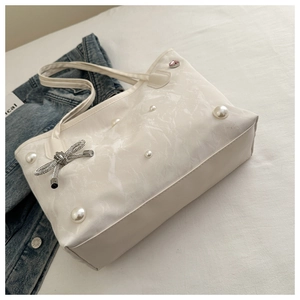 Detail of white tote bag featuring decorative faux pearls and rhinestone bow charm accent
