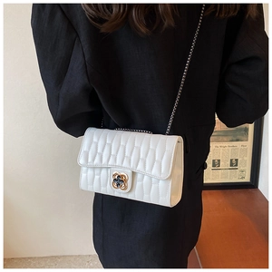 Détail du sac bandoulière blanc embossé avec fermoir fleur dorée sur un costume noir