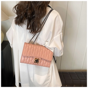 Pink quilted chain bag with floral metal clasp worn over a white shirt by a model