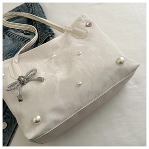 Close-up of cream tote bag with pearl rivets, bow charm and pleated texture detail