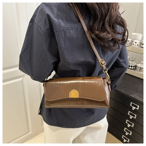 Detail of dark brown leather shoulder bag with gold clasp and sleek minimalist design